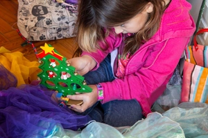 Close-up of child holding a green wooden Christmas tree toy with mini ornaments
