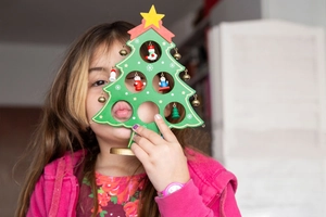 Child holding a green wooden Christmas tree ornament with bells and colorful mini pendants