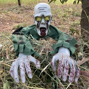 Close-up of crawling zombie Halloween prop with glowing eyes and blood stains in dry grass
