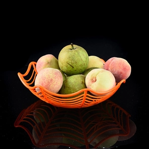 Panier à fruits orange en toile d'araignée avec pêches sur surface réfléchissante