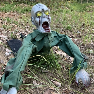 Halloween crawling zombie prop with bloody facial details and green tattered cloth on grass