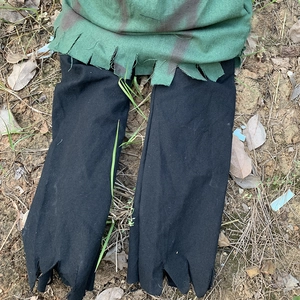 Detail of tattered green top and black jagged pants on leaf ground for zombie costume