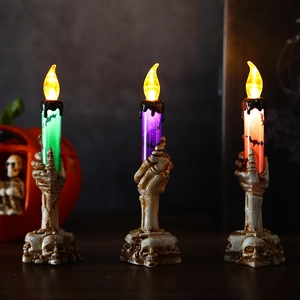 Three Halloween LED candle lights with skull hand bases and bat patterns in a spooky setting