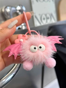 Close-up of pink plush monster pendant with googly eyes and bat wings on a metal clasp