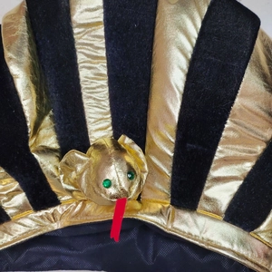 Close-up of golden Egyptian pharaoh hat featuring a detailed snake emblem and stripes