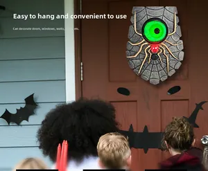 Close-up of Halloween spider doorbell with a glowing green eye on a grey cobweb base