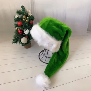Detail of green long-tail plush Christmas hat with white pom-pom near festive tree