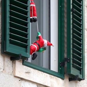 Père Noël grimpant sur une échelle avec sac cadeau vert sur un volet de fenêtre