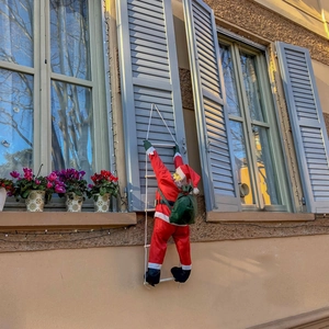 Père Noël grimpant sur une échelle blanche avec un sac de cadeaux sur un volet
