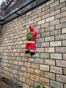 Détail du Père Noël grimpant sur une échelle de corde blanche sur fond de mur en pierre
