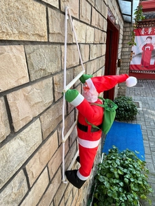 Détail du Père Noël grimpant sur une échelle de corde avec un grand sac cadeau vert