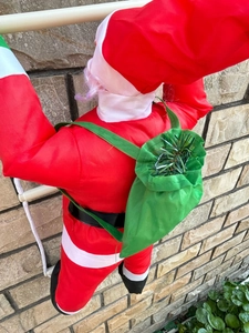 Détail du Père Noël grimpant sur une échelle avec un sac de cadeaux vert sur un mur