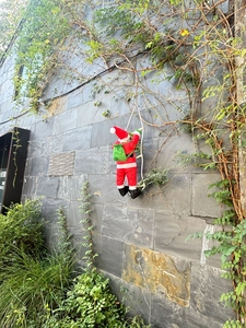 Détail du Père Noël grimpant sur une échelle de corde blanche contre un mur en pierre