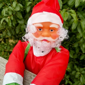 Gros plan du Père Noël décoratif grimpant sur une clôture avec barbe blanche et bonnet