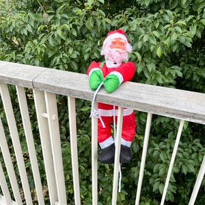 Détail du Père Noël en costume rouge grimpant sur une clôture pour décoration de Noël