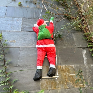 Décoration Père Noël grimpant à l'échelle de corde avec sac à dos sur mur en pierre