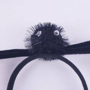 Close-up of black plush soot sprite hair tie with fuzzy texture and cute plastic eyes