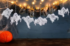 Detail of white gauze ghosts with wooden clips and warm LED string lights on wood