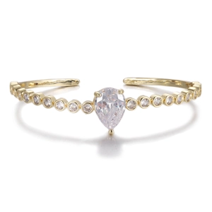 Close-up of golden open bangle featuring a pear-cut clear zircon and bezel-set stones