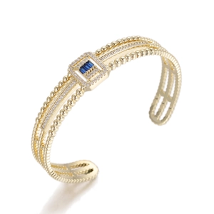 Macro detail of gold open bangle with blue rectangular stones and pave diamonds