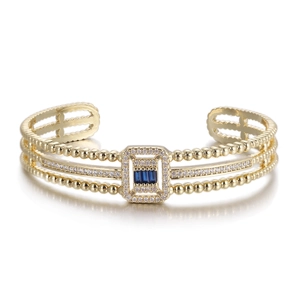 Macro detail of gold triple-layer cuff bracelet with blue rectangle gems and white crystals