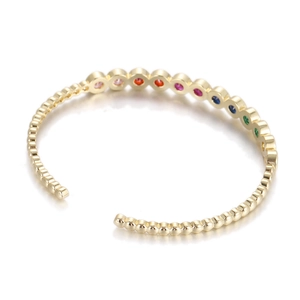 Macro detail of gold-plated open bracelet with rainbow zircon stones and beaded texture