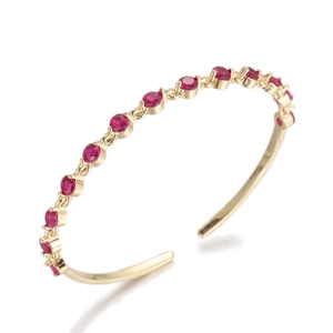 Detail of gold open bangle featuring claw-set red zircons and luxury chain structure