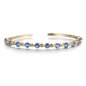 Detail of a gold-plated open bangle featuring round brilliant-cut blue cubic zirconia stones