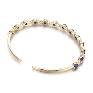 Detailed close-up of C-shaped golden bangle with inlaid round blue cubic zirconia gems