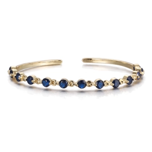 Close-up of golden C-shaped open bracelet with pavé-set round dark blue cubic zirconia stones