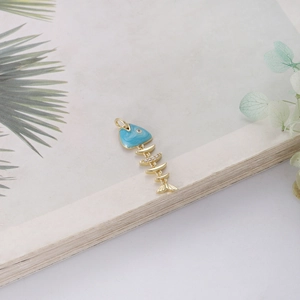 14K gold fish pendant with blue enamel and white zircon accents on book background