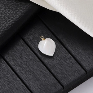 Natural white shell heart pendant with gold bail on a luxury wood and silk background