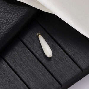 Elegant white teardrop pendant with gold metal clasp on a dark textured background