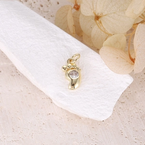 Bohemian gold baby footprint pendant with crystal detail on a natural stone background