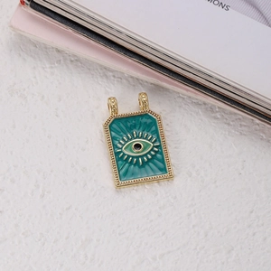 Macro detail of rectangle enamel evil eye charm with turquoise finish and gold beaded edges