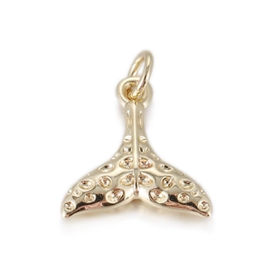 Macro detail of a golden whale tail pendant with textured dots and top hanging ring