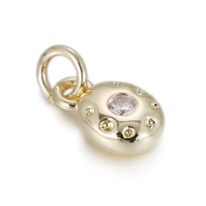 Macro shot of gold oval pendant with clear zircon center and beaded metal texture