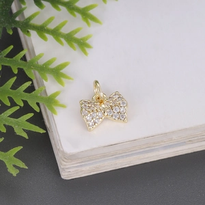 Golden bow pendant with white zircon stones on a decorative white step with cypress