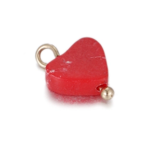 Macro shot of red heart pendant with gold bail and bead on a clean white background