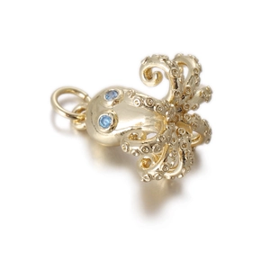 Macro detail of octopus charm with blue gemstone eyes and polished gold texture