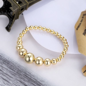 Polished gold beaded bracelet with gradient size beads on a white decorative display plate