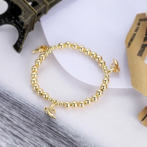Detail of gold beaded bracelet with three polished banana charms on a white display