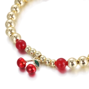 Detail of gold beaded bracelet featuring red translucent beads and a cherry charm