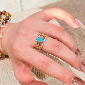 Eleganter offener Goldring mit Filigranmuster und Türkis-Cabochon an einer gepflegten Hand