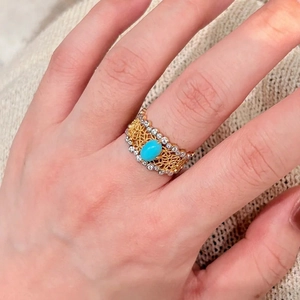 Detailansicht eines vintage goldenen Spitzenrings mit Türkisstein am Finger getragen.