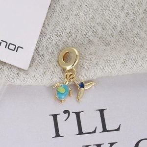 Macro shot of gold-plated sea turtle and whale tail charm with blue enamel details
