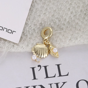 Close-up of golden shell and conch charm pendant with white pearls on white fabric