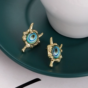 Macro detail of gold-plated evil eye stud earrings on a dark green ceramic display