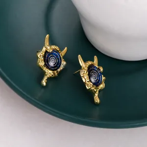 Macro shot of gold devil eye stud earrings featuring blue inlay and fluid horn frame