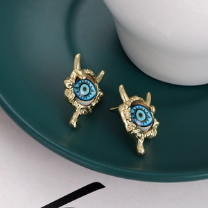 Detailed view of gold evil eye stud earrings with blue accents on a dark ceramic tray